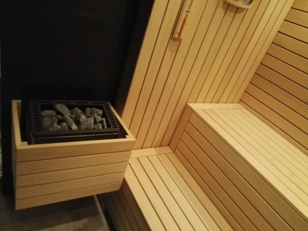 sauna fińska z piecem na kamienie, drewnianymi ławkami i jasną zabudową ścian