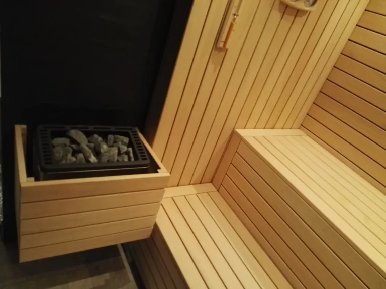 sauna fińska z piecem na kamienie, drewnianymi ławkami i jasną zabudową ścian