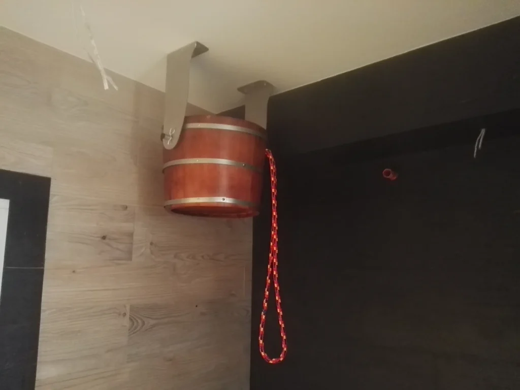 drewniane wiadro prysznicowe w strefie wellness przy saunie i ciemnej ścianie