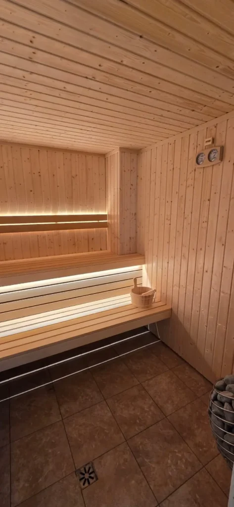 drewniana sauna fińska z ławką, piecem i ciepłym oświetleniem LED