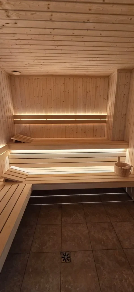 drewniana sauna fińska z ławkami, wiadrem i ciepłym oświetleniem LED