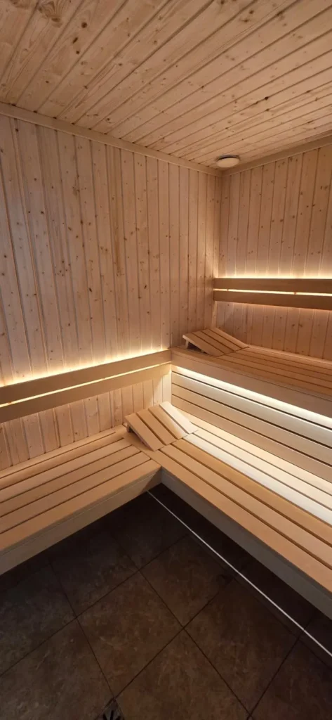 narożna sauna fińska z drewnianymi ławkami, zagłówkami i ciepłym oświetleniem LED