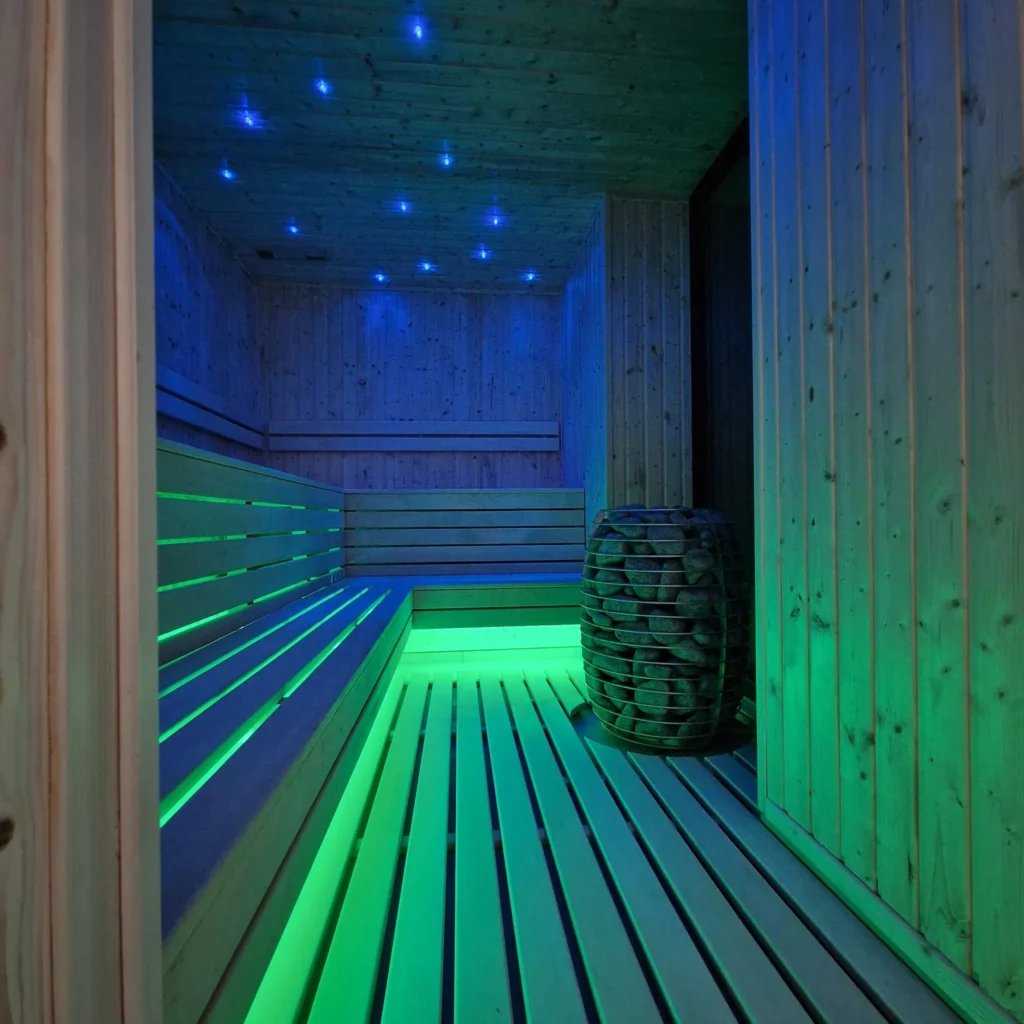drewniana sauna fińska z piecem, ławkami i zielono-niebieskim oświetleniem LED
