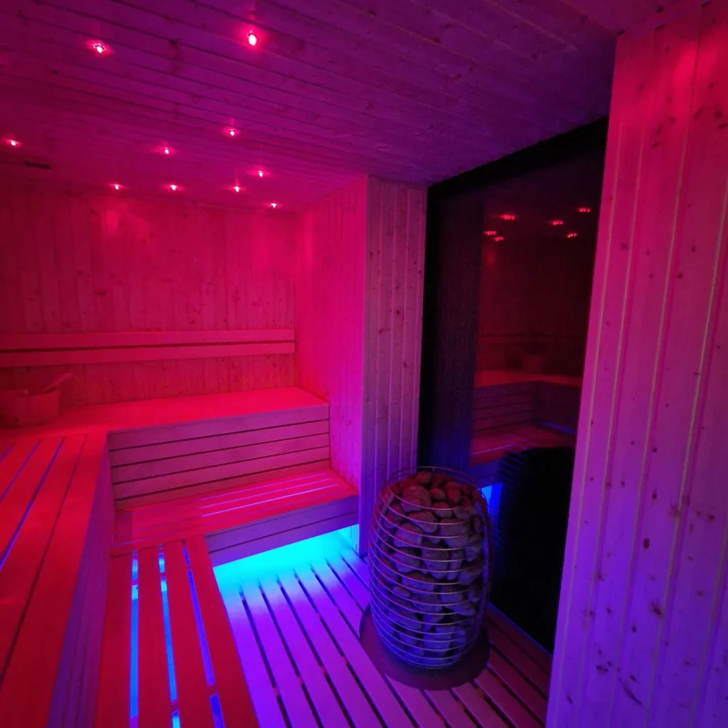 drewniana sauna fińska z piecem, kamieniami i czerwono-niebieskim oświetleniem LED