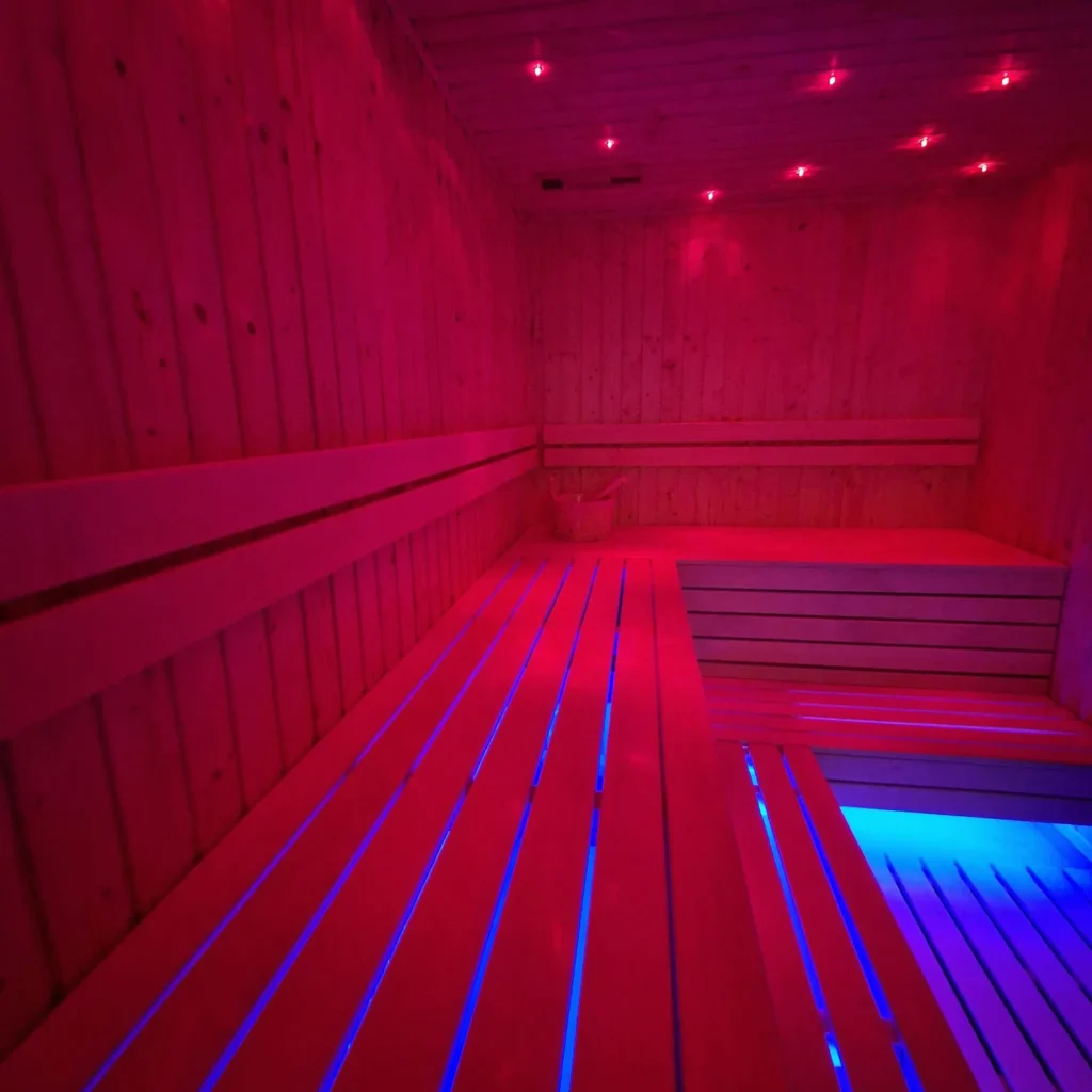 drewniana sauna z długimi ławkami i czerwono-niebieskim oświetleniem