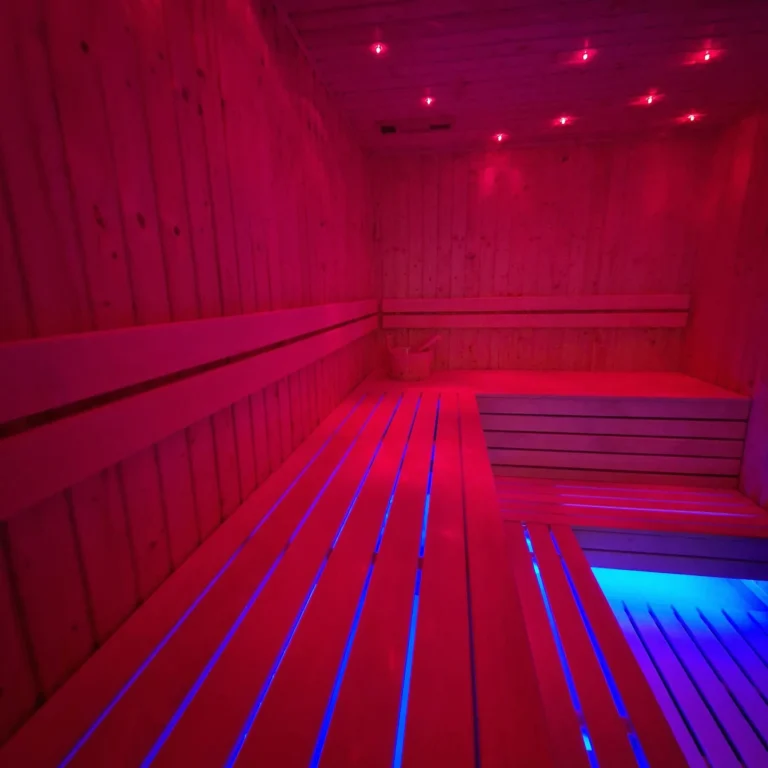drewniana sauna z długimi ławkami i czerwono-niebieskim oświetleniem