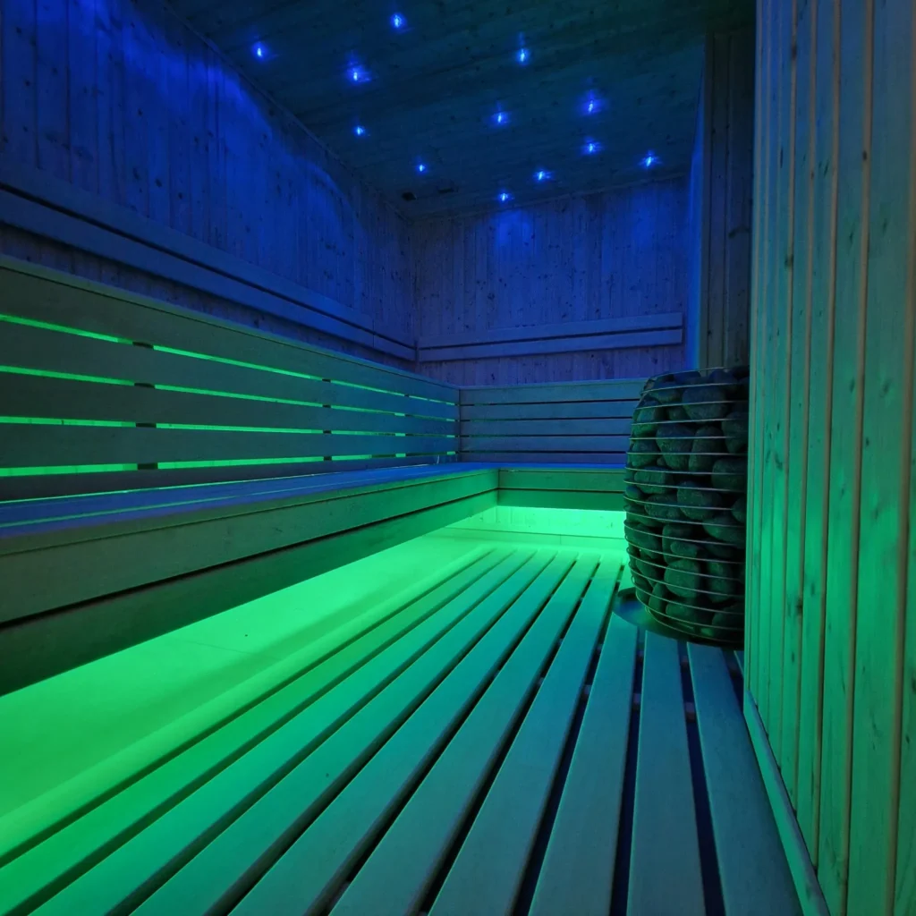 drewniana sauna fińska z piecem i zielono-niebieskim oświetleniem