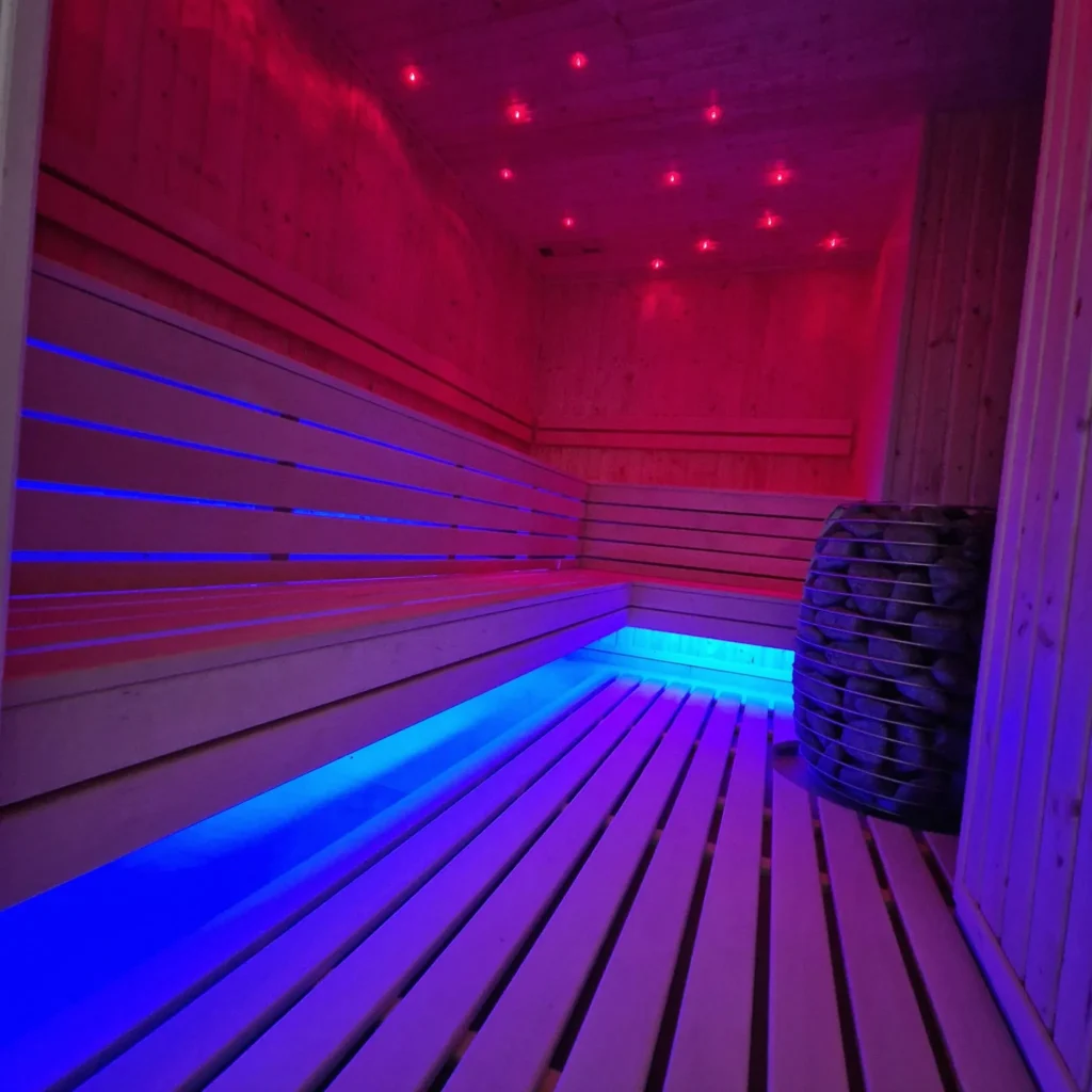 drewniana sauna fińska z piecem i czerwono-niebieskim podświetleniem ławki