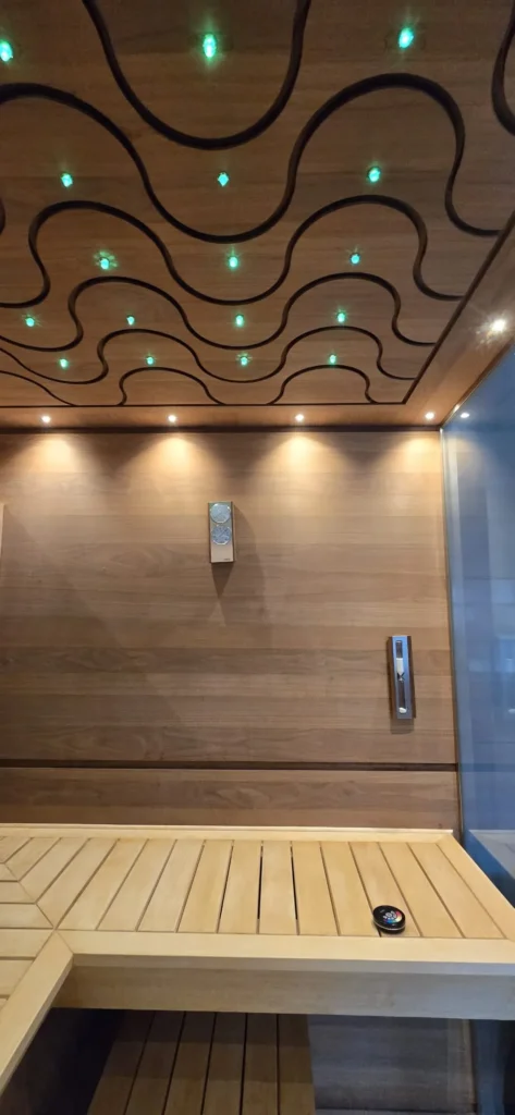sauna z drewnianą ławką, szklaną ścianą i dekoracyjnym sufitem z zielonymi punktami światła