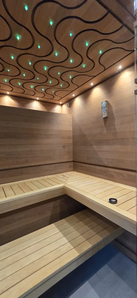 drewniana sauna z narożną ławką, panelem sterowania i falistym sufitem z zielonym światłem